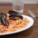 A Chef & Sommelier white bone china oval platter with spaghetti and mussels and a fork on a table.