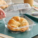 A person's hand holding a Durable Packaging clear hinged lid plastic container with a croissant inside.