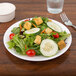 A white Chef & Sommelier bone china plate with a salad of cucumbers and tomatoes with croutons and a fork.