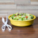A Fiesta Sunflower china bowl filled with salad on a table next to a pair of scissors.