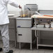 A chef in a white uniform using a Pitco floor fryer in a commercial kitchen.