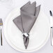 A white plate with an American Atelier silver napkin ring and silverware on it.