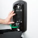 A hand using a black and green rectangular GOJO soap dispenser.