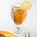 A Libbey Chivalry banquet goblet filled with ice tea and a lemon slice on a table with food.