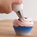 A hand using a Wilton plastic tube to frost a cupcake with pink gel frosting.