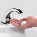 A hand using a GOJO chrome touchless soap dispenser to dispense white soap.