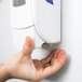 A person's hand pressing a Purell hand sanitizer dispenser on a wall.