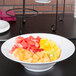 An American Metalcraft round melamine serving bowl filled with fruit on a table.