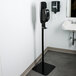 A Purell black touch free hand sanitizer dispenser stand near a sink.
