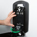 A hand reaching out to a black plastic GOJO True Fit wall dispenser.