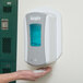 A person holding a GOJO white wall plate with a hand sanitizer dispenser on a wall.