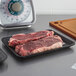 A pair of steaks on a black CKF foam meat tray on a cutting board.