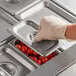A hand wearing a latex glove putting a Choice 1/9 size stainless steel solid steam table pan cover on a tray of tomatoes.