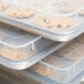 A stack of plastic containers with a white Vollrath bun pan cover over a tray of chocolate chip cookies.