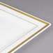 A Fineline Silver Splendor ivory plastic square plate with gold bands on a table.