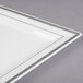 A close-up of a Fineline white plastic square plate with a silver stripe.