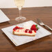 A slice of cheesecake on a Fineline white plastic square plate with silver bands with a fork and a glass of wine.