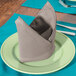 A folded Intedge beige cloth napkin on a plate with a fork.