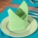 A folded seafoam green Intedge cloth napkin on a plate with silverware.