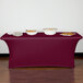 A burgundy Snap Drape Contour table cover on a table with food and white containers.