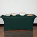 A table with a Snap Drape hunter green spandex table cover and bowls of food on it.