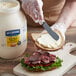 A person spreading Hellmann's mayonnaise on a sandwich with a knife.