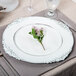 A white Charge It by Jay plastic charger plate with an embossed flower design.