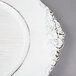 A white Charge It by Jay plastic charger plate with an ornate white border.