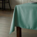 A table with a seafoam green rectangular tablecloth on it.