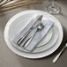 A white Charge It by Jay rattan charger plate with silverware and a napkin on it.