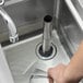 A hand holding a glass in a sink with a 7 1/2" silver overflow pipe in the drain.