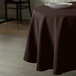 A round brown table with a brown Intedge tablecloth on it.