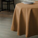 A round brown table with a beige Intedge tablecloth and a plate on it.