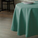 A table with a teal Intedge round tablecloth and a white plate on it.