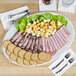 A Tuxton Alaska china platter with lettuce, cheese, and meat on it.