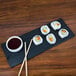 A plate of sushi with chopsticks and soy sauce on a black faux slate melamine display board.