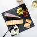 A Madison Avenue faux slate melamine display board with cheese, grapes, and wine on a table.