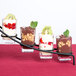 A black roller coaster dessert shot display stand holding four glasses of desserts with fruit and chocolate.