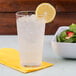 A clear GET plastic tumbler of water with ice and a lemon slice on a yellow napkin.