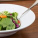 A Minski white melamine bowl filled with salad on a table with a fork.