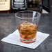 A GET Revo old fashioned glass filled with brown liquid and ice on a napkin.