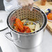 A person using a Vollrath Wear-Ever fryer pot to cook lobster and corn.