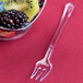 A clear WNA Comet plastic tasting fork in a bowl of fruit.