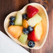 An Eco-gecko palm leaf heart shaped plate filled with fruit on a table.