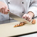 A chef using a Mercer Culinary Genesis chef knife to cut meat on a cutting board.