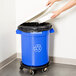 A person opening a blue Continental Huskee recycling trash can with a blue lid.