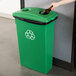 A person's hand throws a bottle into a green Continental recycling bin with a recycle symbol on it.