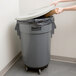 A person putting a large box into a grey Continental Huskee trash can with a white lid.
