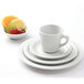 A Tuxton Colorado bright white narrow rim saucer with a white cup on it, next to strawberries and lime slices.