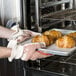 A pair of hands wearing Cordova hot mill gloves holding a tray of croissants in an oven.